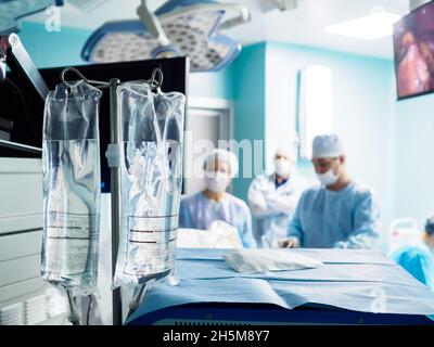 Selective focus on clear infusion bags in the operating room. Saline bags for dropper in the hospital. Surgery on a blurred background. The inscription on the bag in Russian means: Sodium Chloride Stock Photo