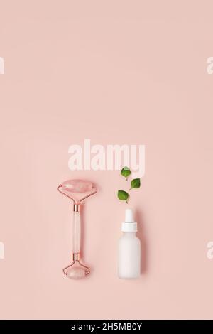 Beautiful composition of white mockup serum bottle, pink quarts stone face roller and fresh leaves on pink background. Natural cosmetics concept. Creative trendy cosmetics flat lay with copy space. Stock Photo