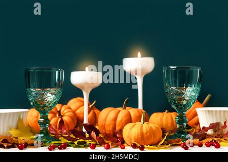 Mockup green vintage plates, goblets, candles, maple leaves, pumpkins and cranberries on dark green. Autumn composition with copy space. Halloween and thanksgiving concept. Stock Photo
