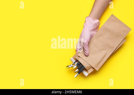 Female hand holding paper bag with manicure equipment on yellow background Stock Photo