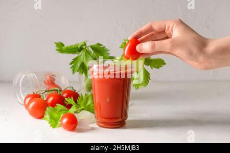 Woman decorating glass of bloody mary with cherry tomato at table Stock Photo