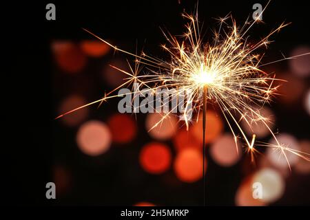 Burning Christmas sparkler against blurred lights Stock Photo