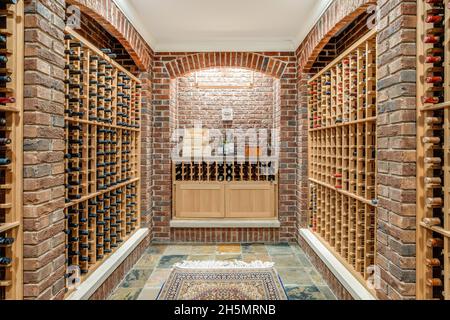 A large walk-in wine cellar in a luxury home with brick walls and wooden wine racks. Stock Photo