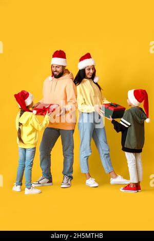 Little children giving Christmas presents to their parents on yellow background Stock Photo