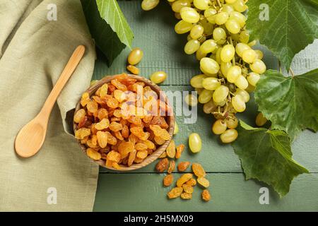 Bowl with tasty raisins and ripe grapes on color wooden background Stock Photo