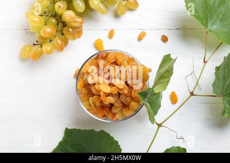 Glass bowl with tasty raisins, ripe grapes and branch on light wooden background Stock Photo