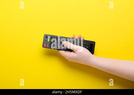 Woman pressing button on TV remote controller on yellow background Stock Photo