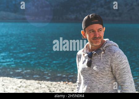 Man standing in front of mountain lake with ball cap on looking away  Stock Photo