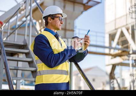 Male engineer using mobile phone outdoors at factory Stock Photo