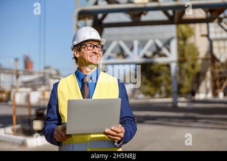 Joyful male worker using laptop outdoors at factory Stock Photo