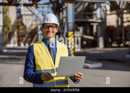 Joyful male engineer using notebook outdoors at factory Stock Photo