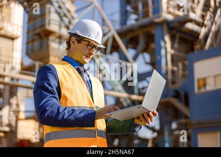 Male engineer working on laptop outdoors at factory Stock Photo
