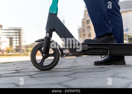 Close up of legs man in suit riding electric scooter in city. Unknown businessman in classic suit ride on electric mobile scooter. Modern eco friendly Stock Photo