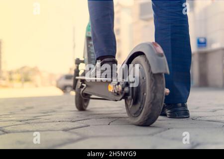 Low Section Of A Businessman Standing On Electric Scooter At Street. alternative mode of transport Stock Photo
