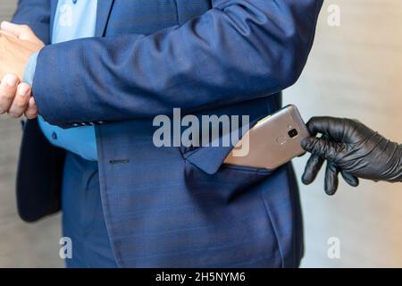 A gloved hand pulls out a mobile phone from a businessman's pocket. The concept of pickpocketing. The pickpocket is working. Stock Photo