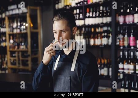 Sommelier man in apron listens to aroma of red wine, sniffs cork. Stock Photo