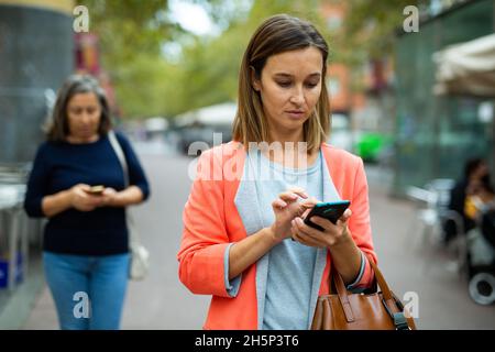 Focused young business woman using smartphone while walking outoors Stock Photo