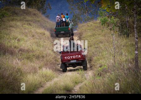 A couple of old model Toyota Hilux trucks going up a hill on an offroad track in Central Province, Papua New Guinea Stock Photo