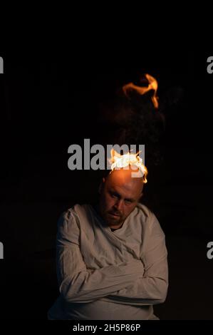 Bald man in a straitjacket with a burning head on a dark background. Stock Photo