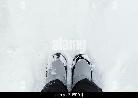Feet snow top view. Winter gray boots stand on white snow. Textured background. Women's suit black pants and boots for walking, hiking, trekking. The Stock Photo