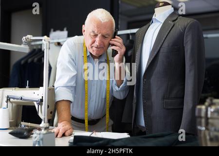 Professional tailor man talking on mobile phone and making notes in notebook Stock Photo