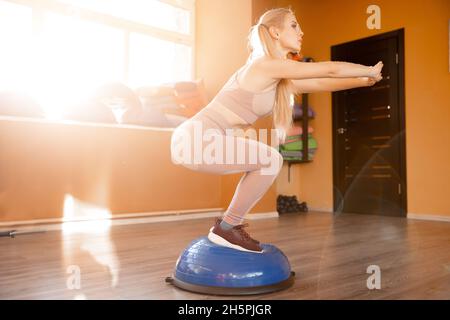 Young woman trainer making squats on bosu balance ball sunlight. Stock Photo