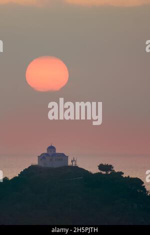 The small church of Agios Nikolaos under the orange sun at sunset. In the port of Myrina on the island of Lemnos Stock Photo