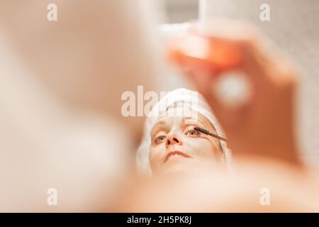 Adult woman applying mascara on eyelash in bathroom. Stock Photo