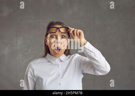 Amazed woman raises her glasses looking into the camera with a distrustful expression. Stock Photo