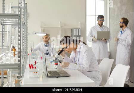 Young smart woman examines test samples with a microscope in a modern medical laboratory. Stock Photo