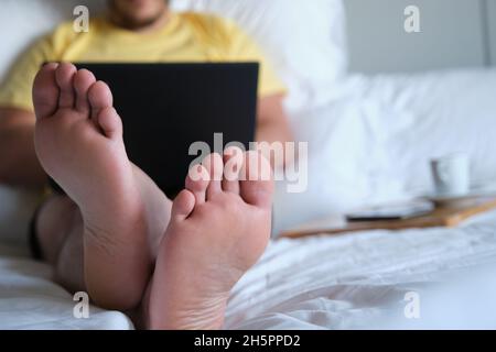 Unrecognizable man working with laptop in an hotel room bed. Stock Photo