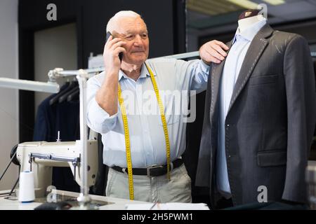 Professional tailor communicates with the client on mobile phone and takes notes in notebook Stock Photo