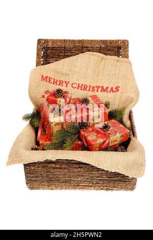 Christmas wrapped gifts with red ribbons on a jute sack with text 'Merry Christmas', decorated with pine cones and pine twigs in a wicker basket, isol Stock Photo