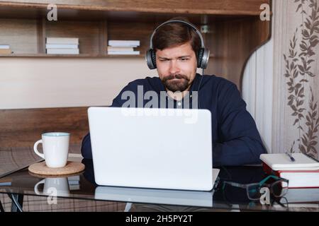 Happy male student online teacher wear headphone talk video calling, looking at laptop computer screen, do conference chat communicate with skype tutor, distance education e learning course at home Stock Photo
