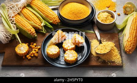 Corncobs and corn groats on gray background. Harvest food concept. Stock Photo