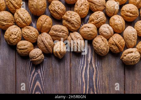 many walnuts with shells randomly scattered on brown wooden surface with copy space at bottom of picture Stock Photo