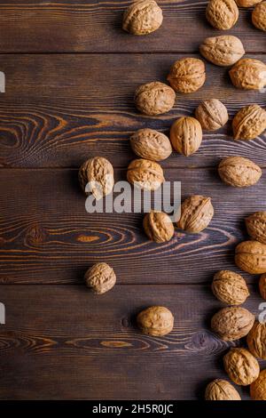 many walnuts with shells randomly scattered on brown wooden surface Stock Photo