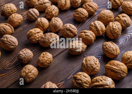 many walnuts with shells randomly scattered on brown wooden surface Stock Photo