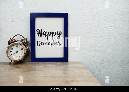 Happy December typography text and alarm clock on wooden table and white wall background Stock Photo
