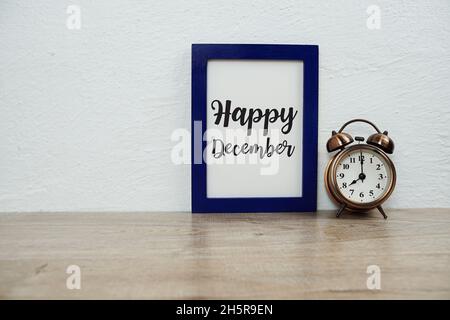 Happy December typography text with alarm clock on wooden table and white wall background Stock Photo