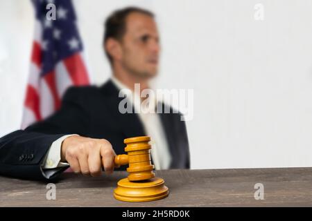 Man judge holding wooden gavel on court room with usa flag in background. Stock Photo