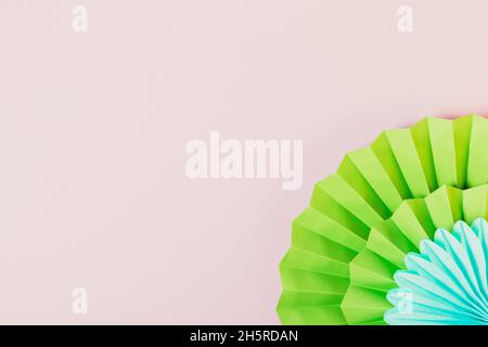 Holiday background with paper decorations. Green and blue origami fans on light lilac backdrop with copy space Stock Photo