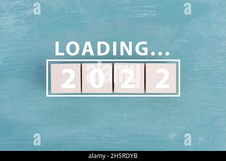 2022 is standing in white colored letters on wooden cubes, the word loading is standing above, blue background Stock Photo