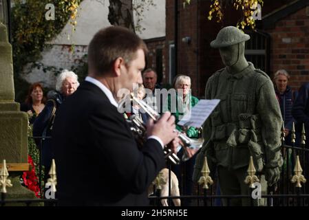 Syston, Leicestershire, UK. 11th November 2021. The last post is played near a life size knitted soldier during Armistice Day commemorations at the Syston War Memorial. Credit Darren Staples/Alamy Live News. Stock Photo