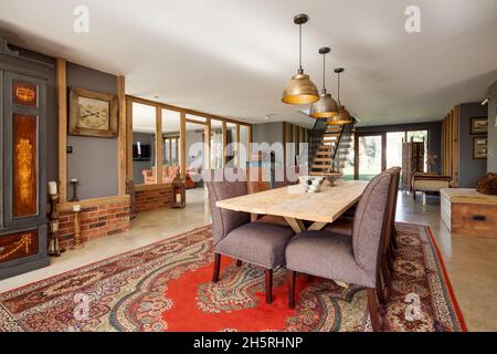 Suffolk, England - March 2018: Dining hall within converted barn dominated by a large dining table with eight chairs illuminated by sunshine Stock Photo