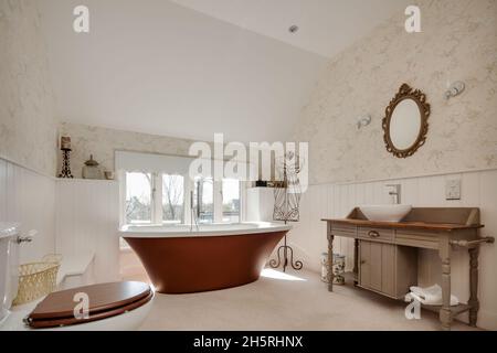 Suffolk, England - March 2018: Domestic bathroom WC with ceramic Basin on wooden plinth, half clad timber walls and freestanding bath tub. Stock Photo