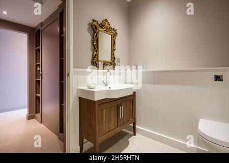 Suffolk, England - March 2018: Domestic WC cloakroom and dressing area with ceramic basin on wooden plinth and ornate framed mirror Stock Photo