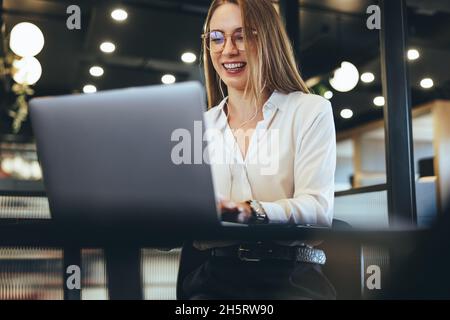 Female entrepreneur taking a video call in an office. Happy young businesswoman smiling while using a laptop and wearing earphones. Cheerful businessw Stock Photo