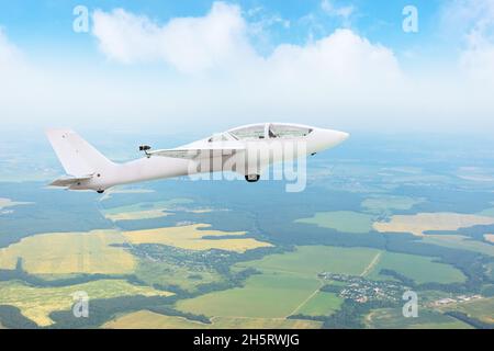 Glider flying high in the sky over fields and forests, aerial view Stock Photo