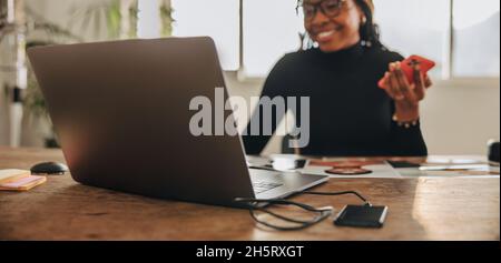 Happy creative designer taking a phone call in her home office. Creative young woman smiling while sitting at her desk. Freelancer communicating with Stock Photo